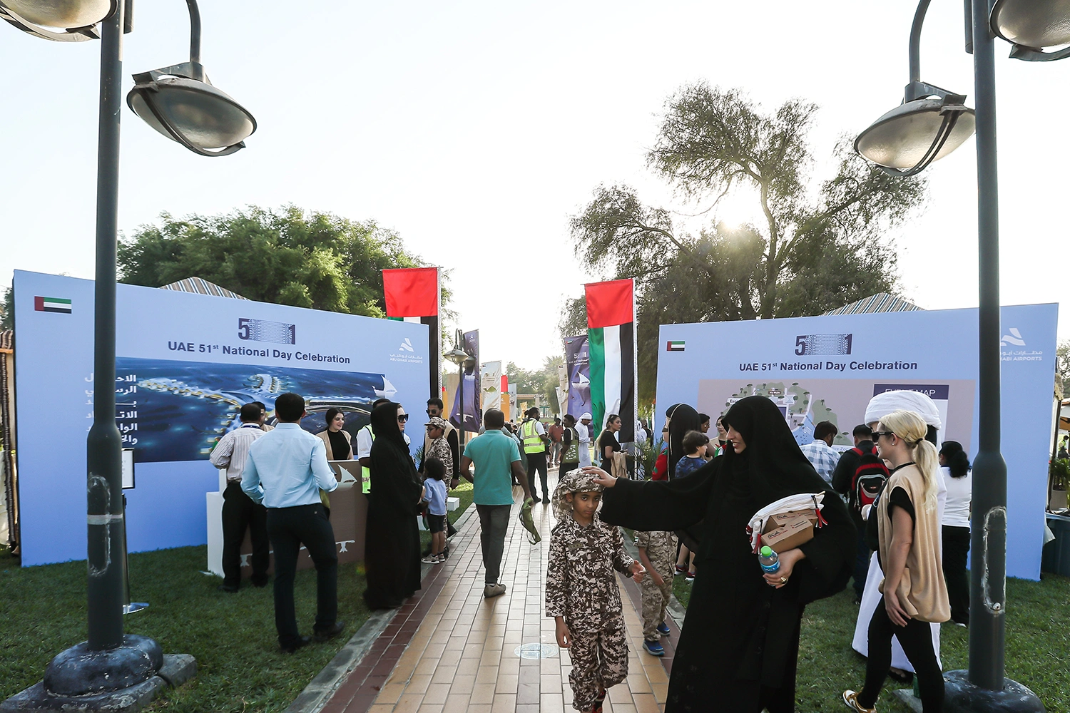 Families and guests walking along brick pathway surrounded by outdoor exhibition walls in Abu Dhabi garden