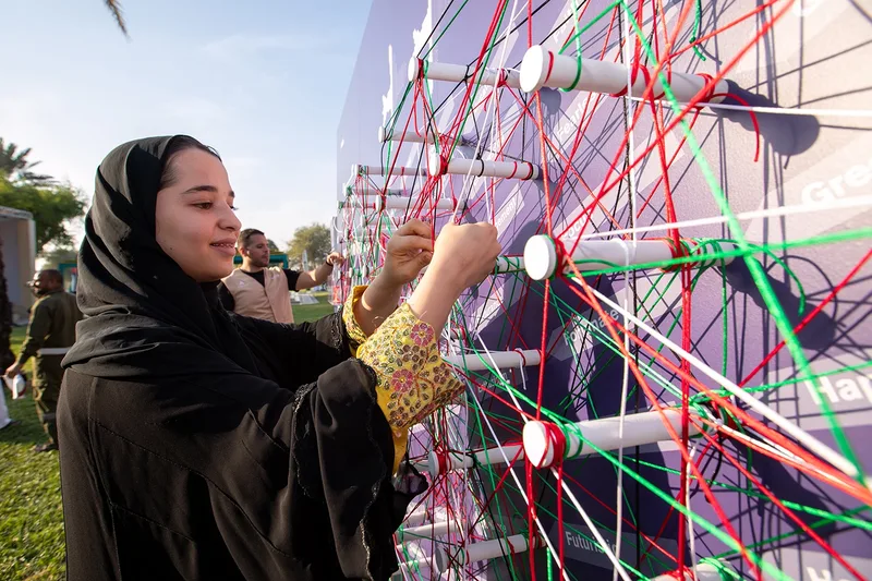 Visitor threading green yarn through pegs on custom interactive string art board in outdoor park