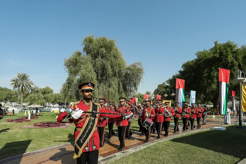 Abu Dhabi Police marching band in red ceremonial uniforms marching through outdoor park venue