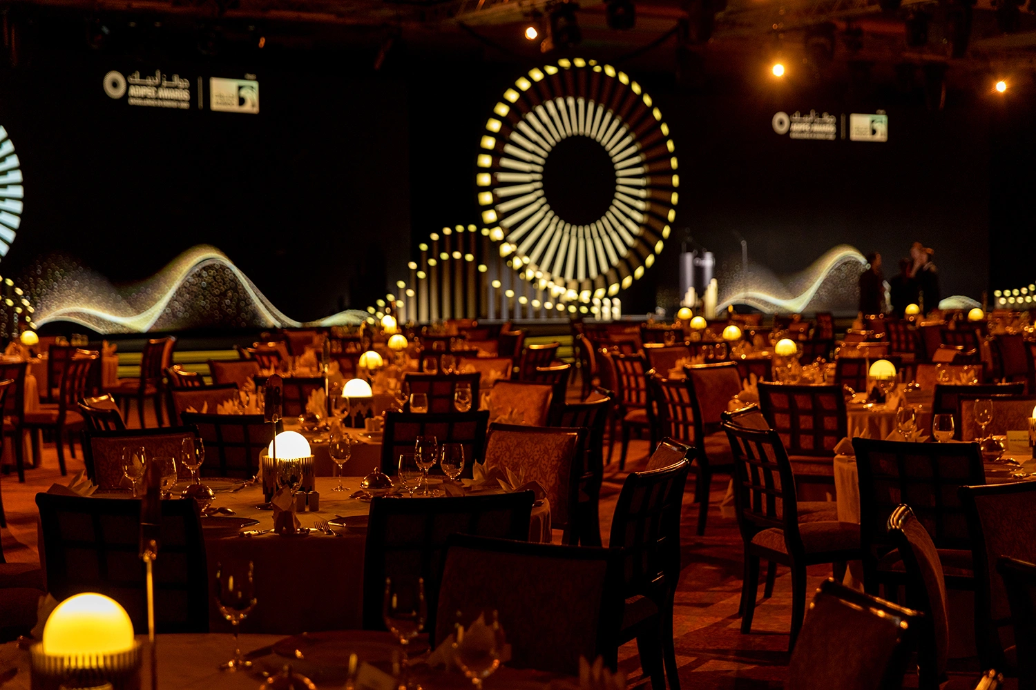 ADIPEC Awards 2022 ballroom dinner setup with illuminated tables and a dramatic circular stage backdrop.