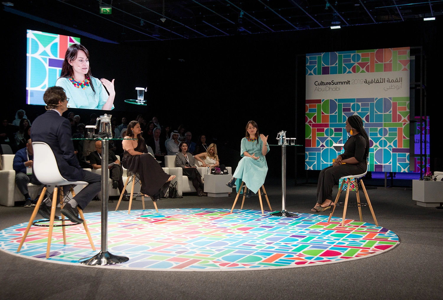 Evolution Events circular panel stage with branded flooring, live screen and audience seating