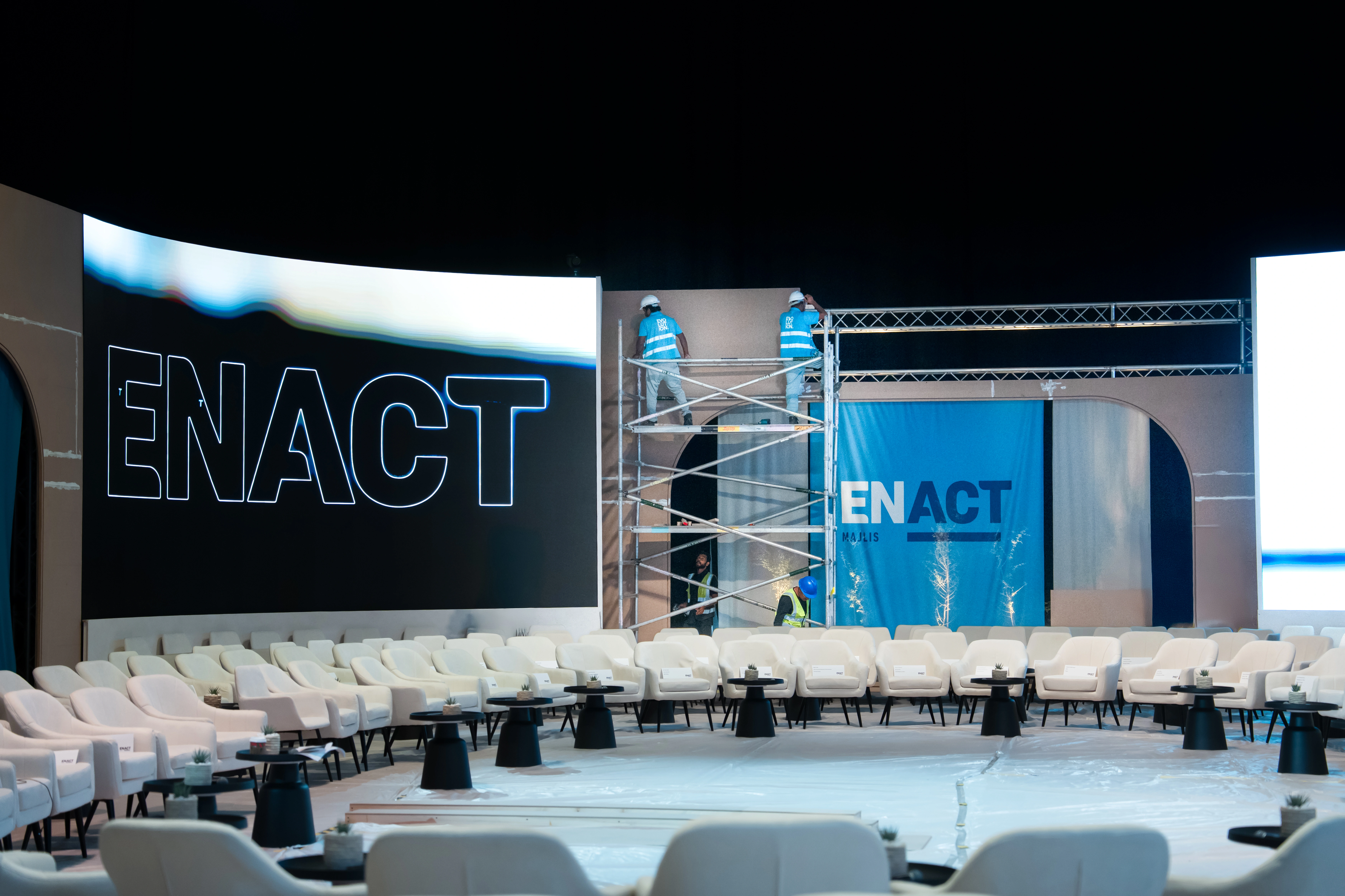 ENACT Majlis event venue during installation, with technicians assembling the stage backdrop, LED screens and circular seating layout