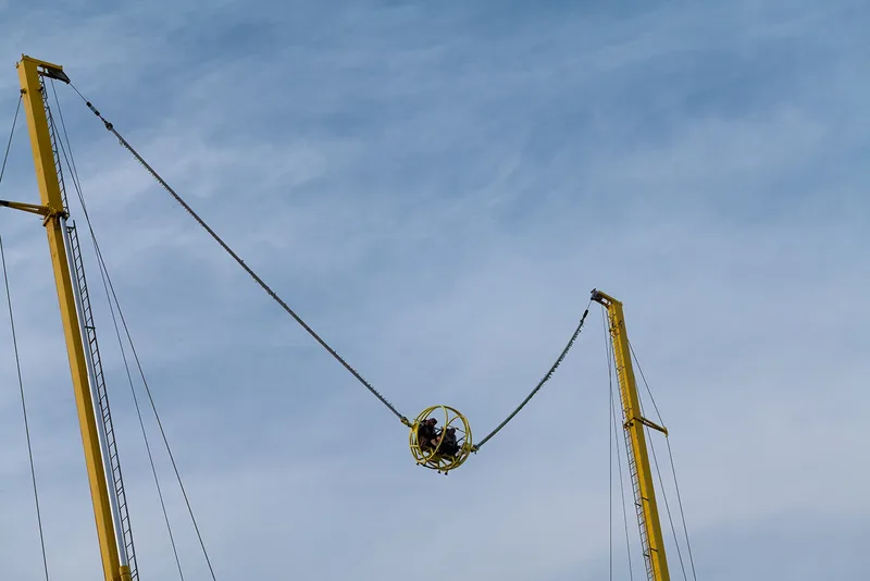 High-adrenaline slingshot amusement ride suspended against blue sky at Diriyah Oasis event site