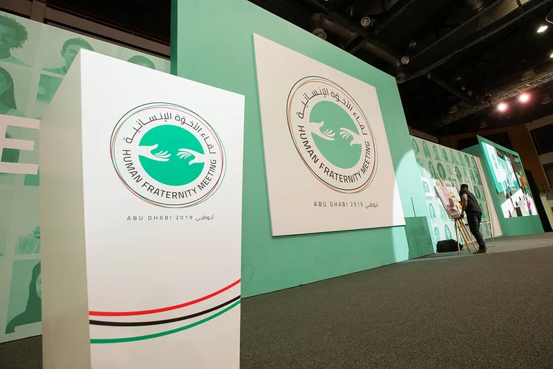 Human Fraternity Meeting stage with bilingual branded scenic panels, live artwork and integrated event screens