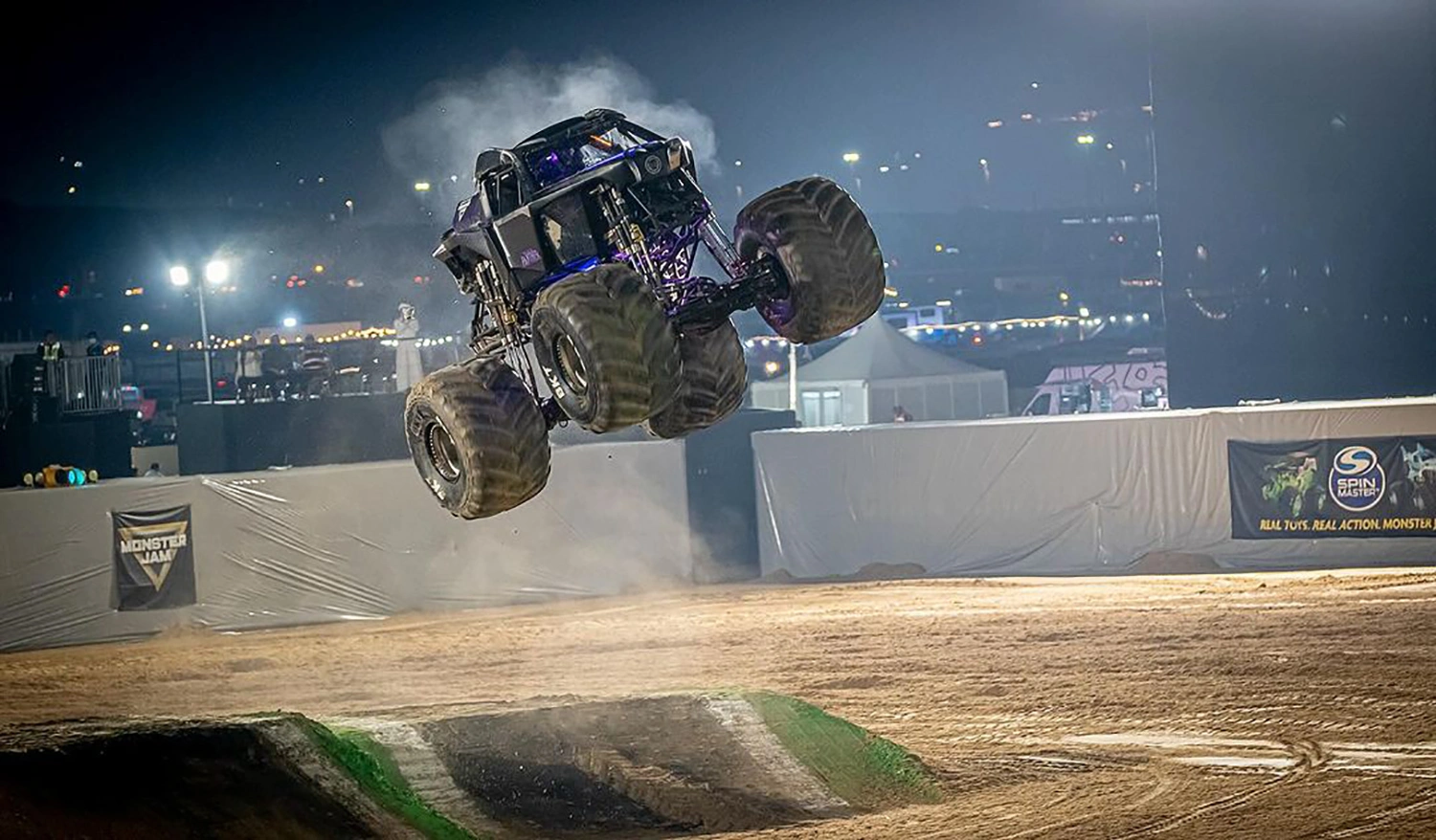 Monster trucks performing aerial stunts on custom built dirt jump ramps in Liwa arena